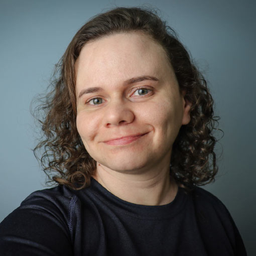 This is a picture of Juliana Moreira, aka Jujuqui. A woman in ther late thirties, with dark blonde curled hair, white skin and green eyes. In the picture, she is smiling at the viewer, with her mouth closed.